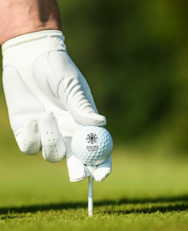 Ein Golfer mit Golfhandschuh platziert einen Ball auf einer Abschlaghilfe.