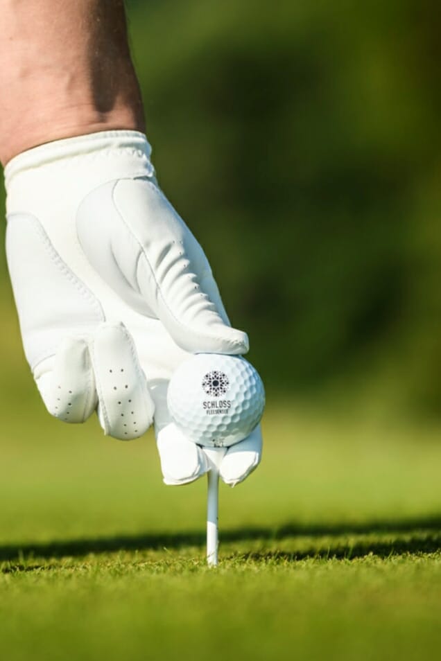 Ein Golfer mit Golfhandschuh platziert einen Ball auf einer Abschlaghilfe.