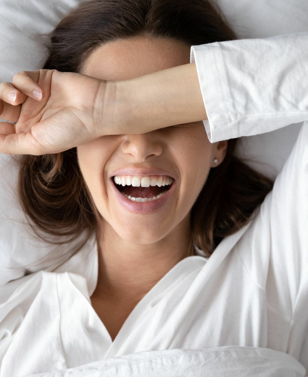 Eine Frau liegt und hat den Arm über ihren Augen, während sie lacht.