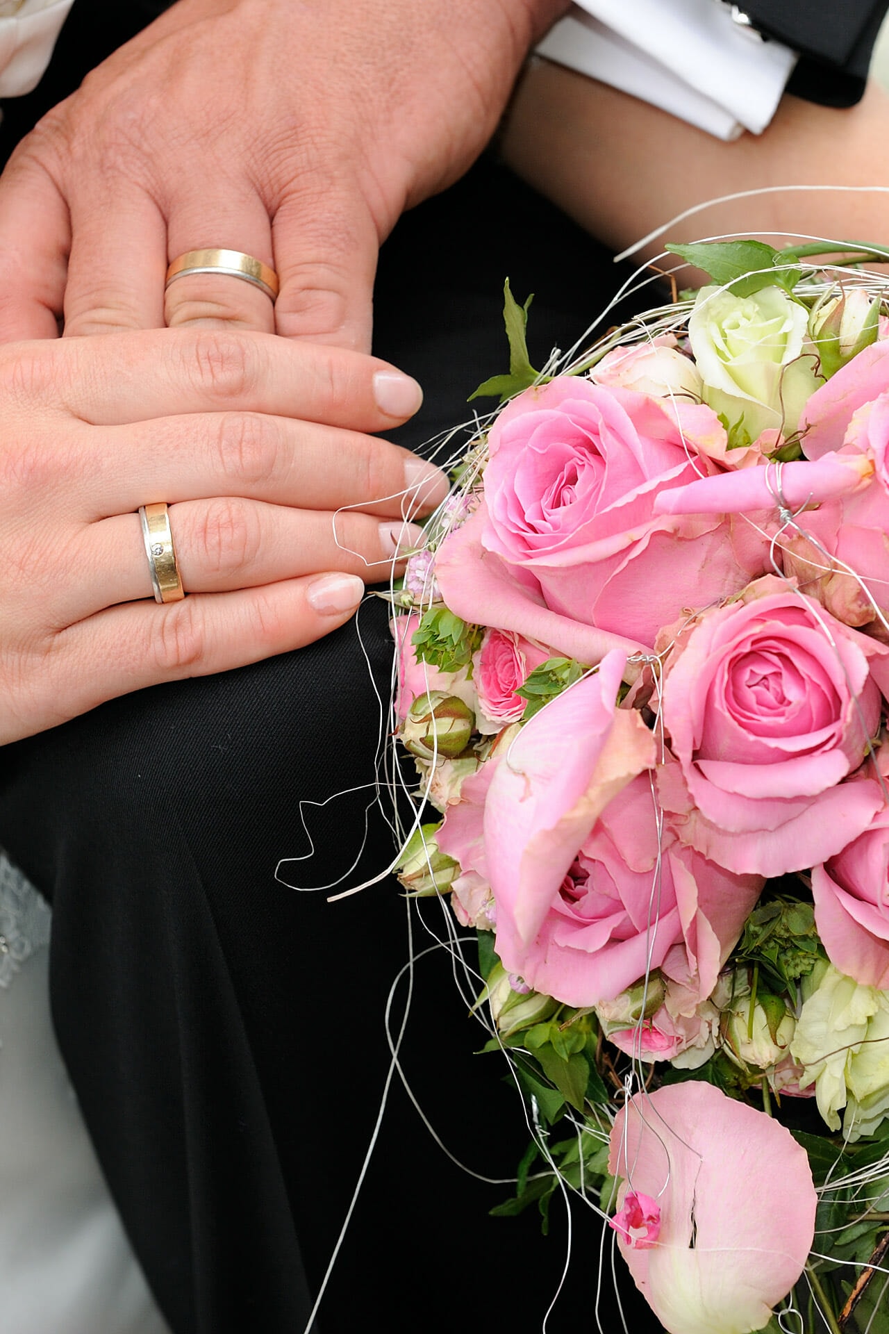 Hände mit Eheringen und ein rosa Blumenstrauß.