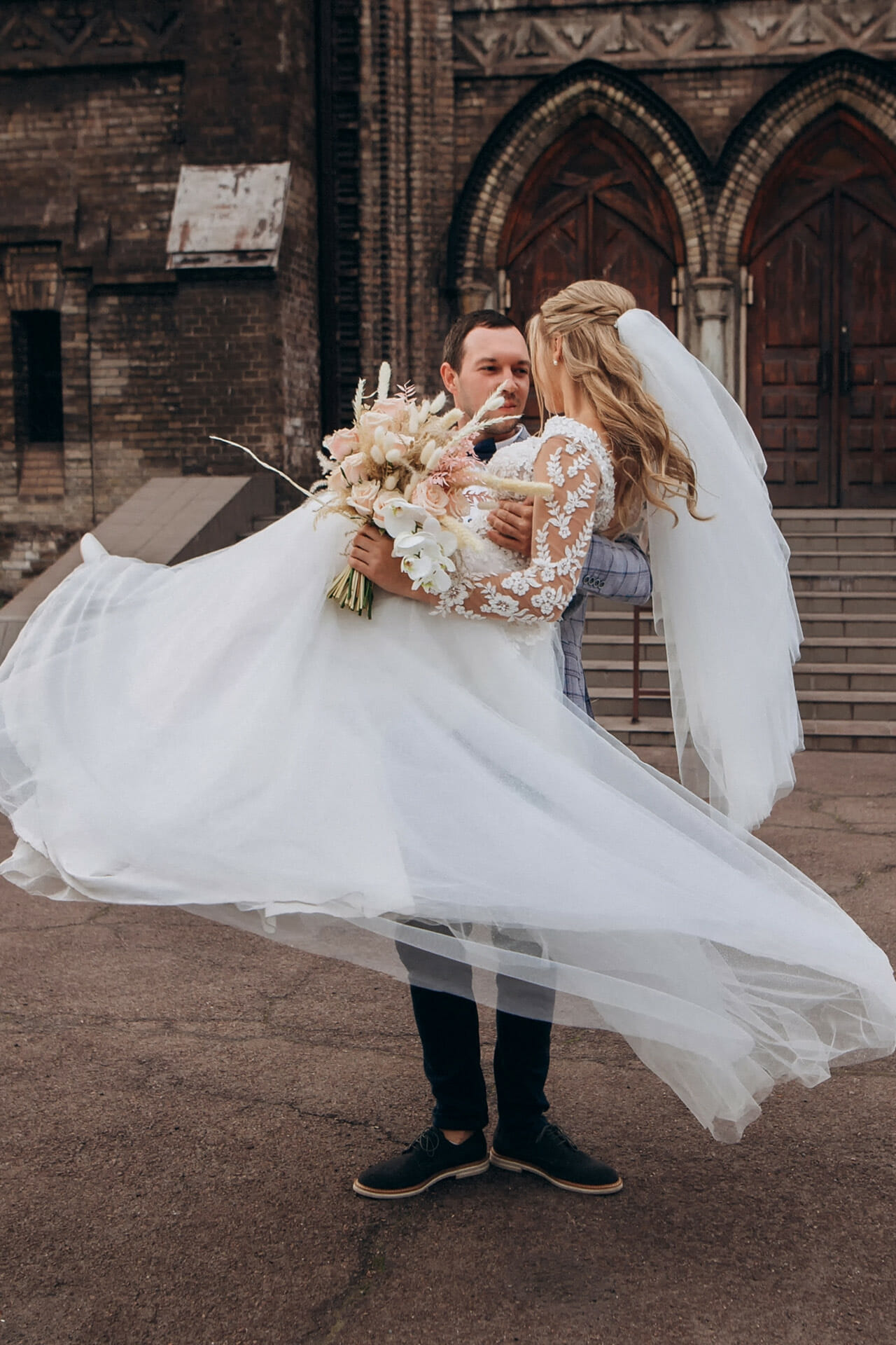 Ein Bräutigam hat die Braut auf dem Arm und das weiße Kleid bauscht sich auf.